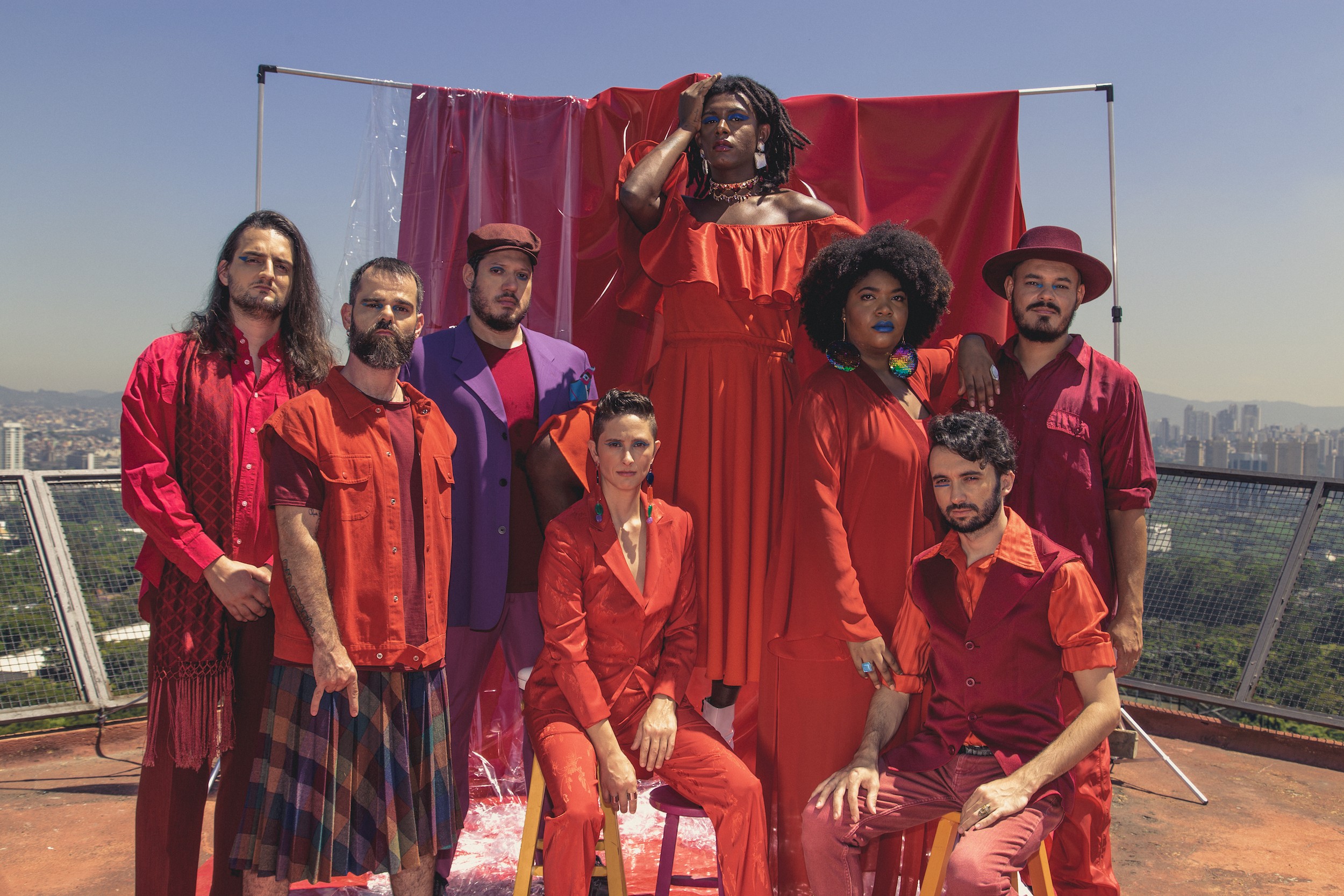 Fotografia mostra integrantes do conjunto "Liniker e os Caramelows"reunidos trajando vestes vermelhas.