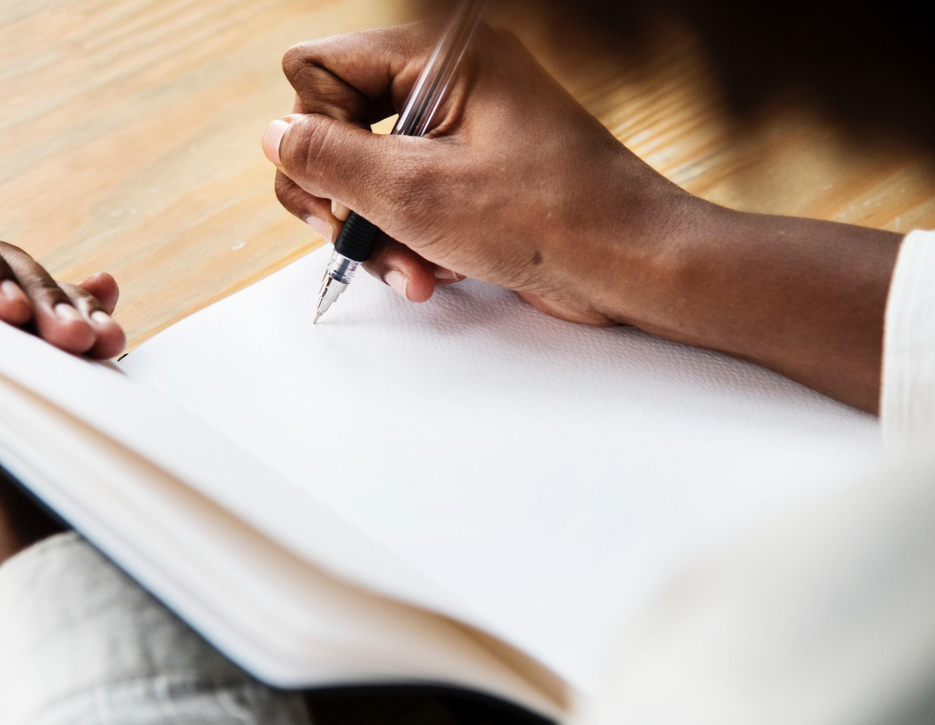 Mão de uma pessoa negra escreve sobre caderno