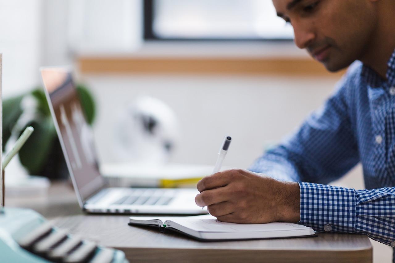 foto de homem negro segurando lápis e escrevendo em um caderno