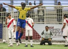 Jogador de Futebol de 5 com a camisa da Seleção Brasileira, pulando, de braços abertos dom uma venda nos olhos.